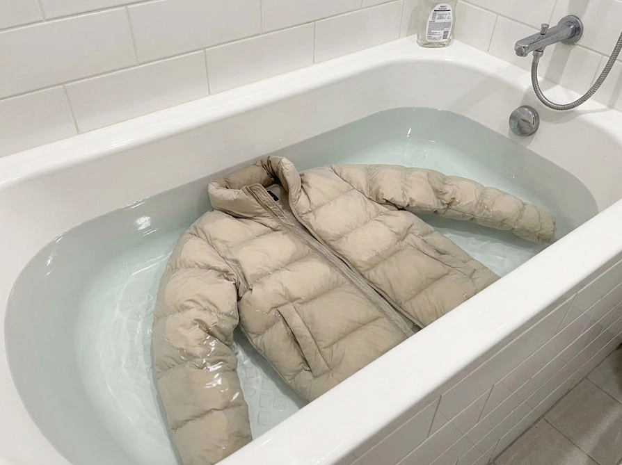 浴槽の透明な水でダウンジャケットをすすいでいる様子