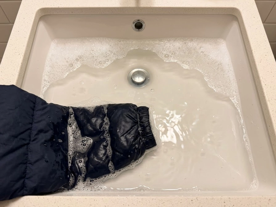 洗面器のぬるま湯にジャケットの一部を浸して予洗いしている様子