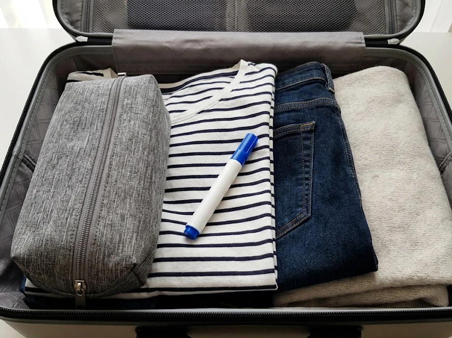 旅行カバンの中に、ポーチや衣類と一緒にダイソーの携帯用染み抜きペンを綺麗にパッキングしている様子