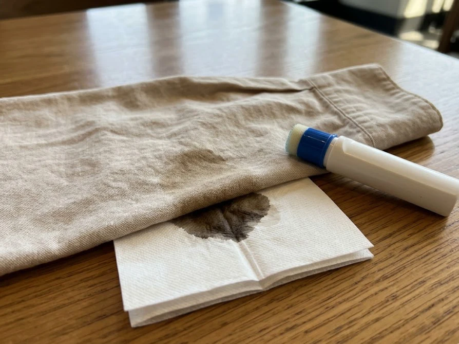 カフェで衣類の汚れの下にティッシュを当て布として敷き、ダイソーの携帯用シミ抜きで応急処置をする様子