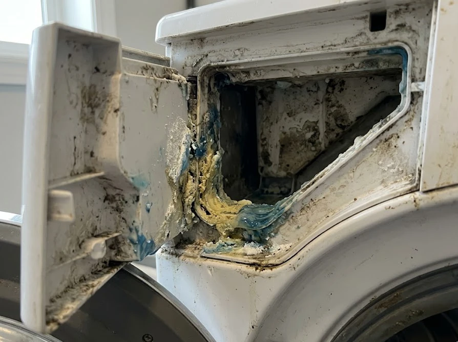 洗濯機の洗剤投入口に、青い液体洗剤がドロドロに固まって残っている様子