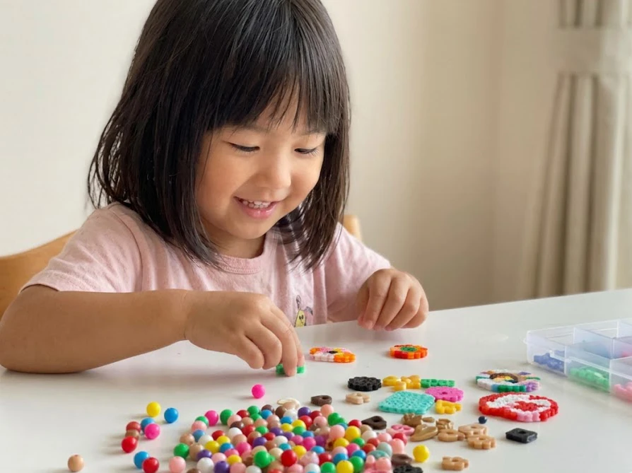 テーブルの上に並べられたカラフルなビーズを嬉しそうに選ぶ子供
