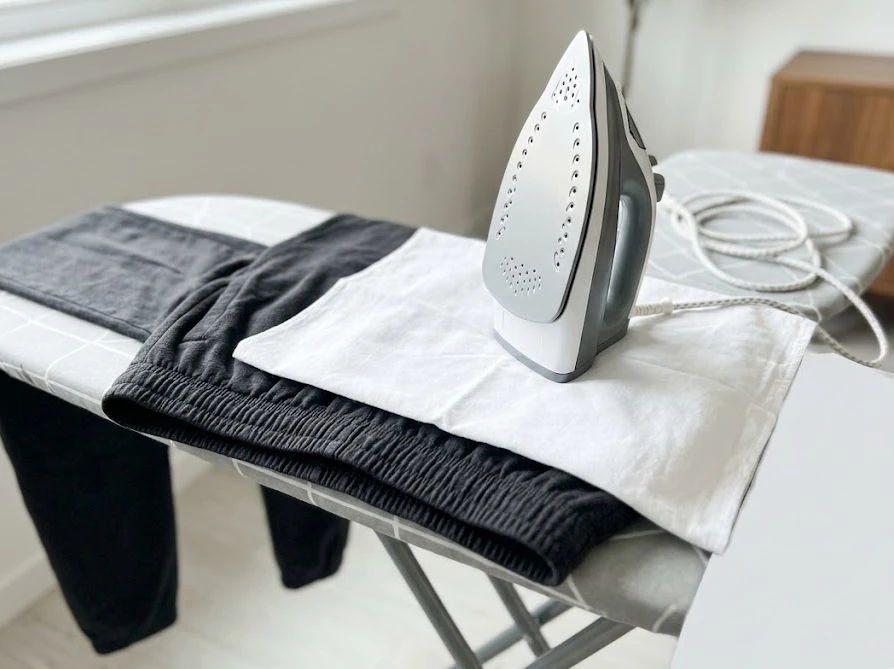 ズボンのゴム部分に直接熱が当たらないよう、綿の当て布をしてアイロンで素早く乾燥させている様子。