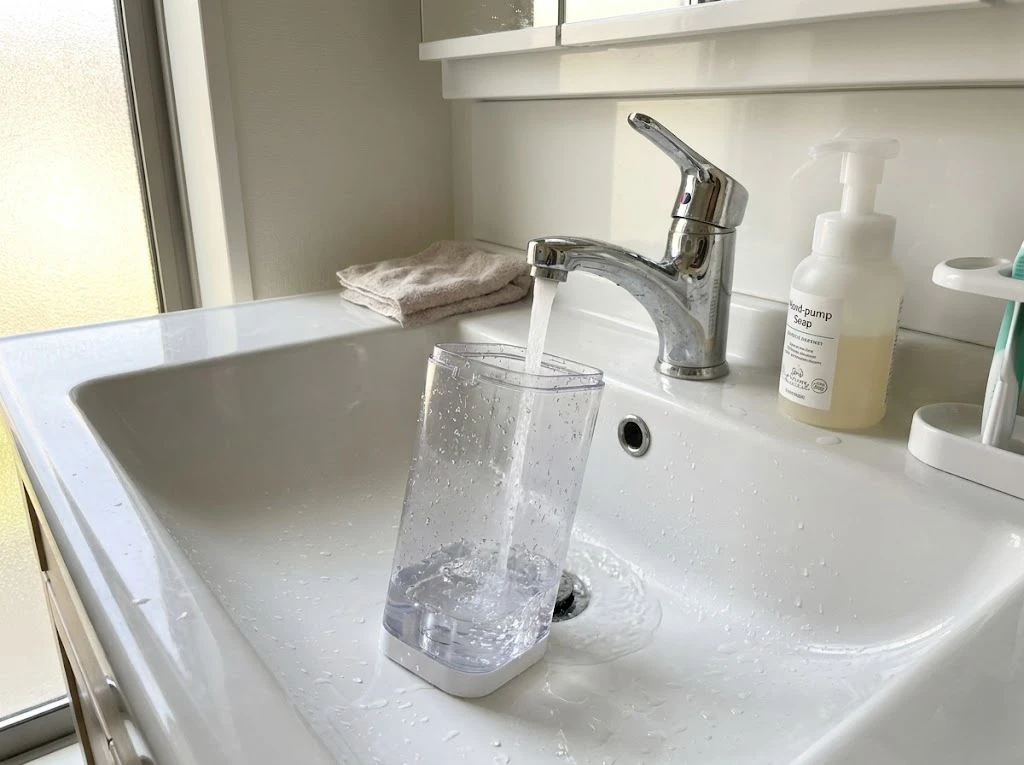 洗面台で洗濯機の自動投入タンクをお湯でメンテナンスする様子