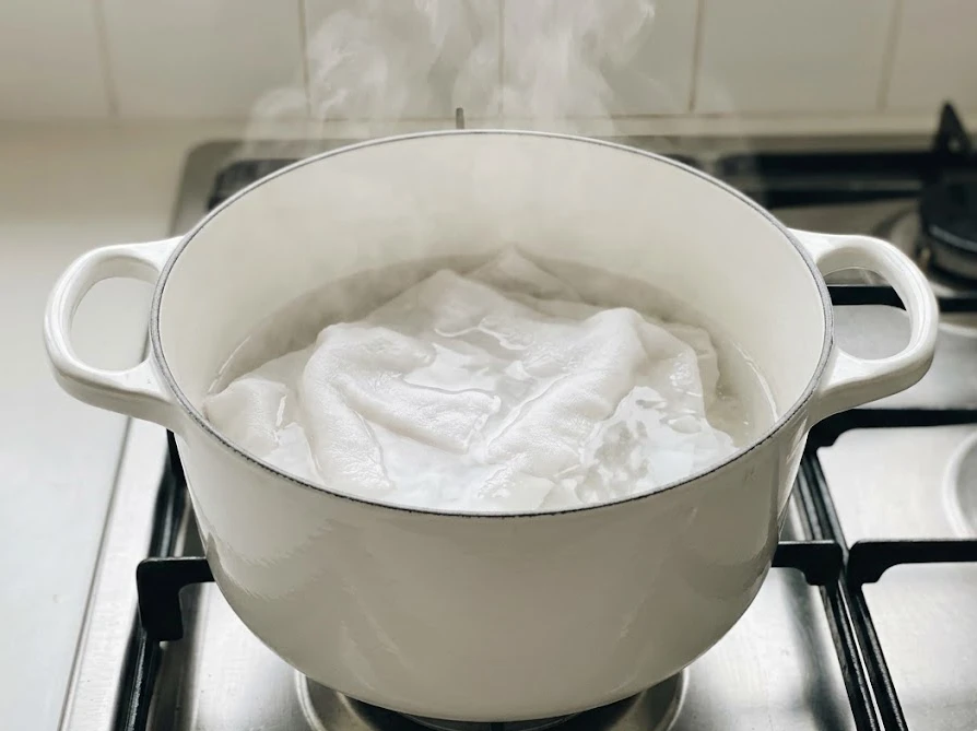 キッチンのコンロでホーロー鍋を使って衣類を煮洗いしている様子