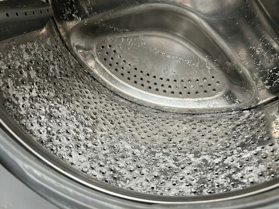 洗濯槽の内側にこびりついた、石鹸カスによる白くてザラザラした不快な汚れの様子