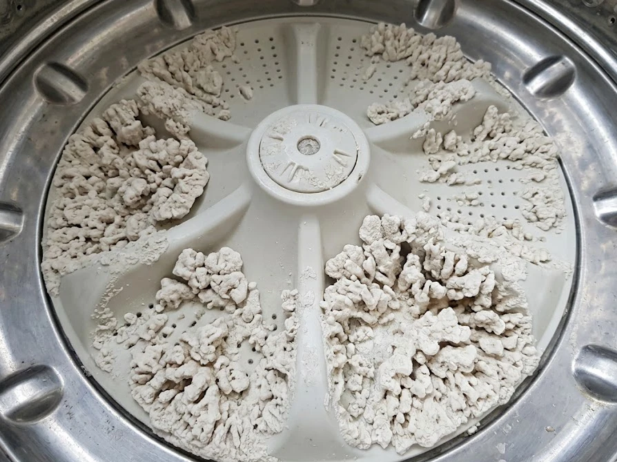 アルカリ性洗剤の溶け残りが原因で、洗濯槽の底に石のように固まった白い結晶汚れ