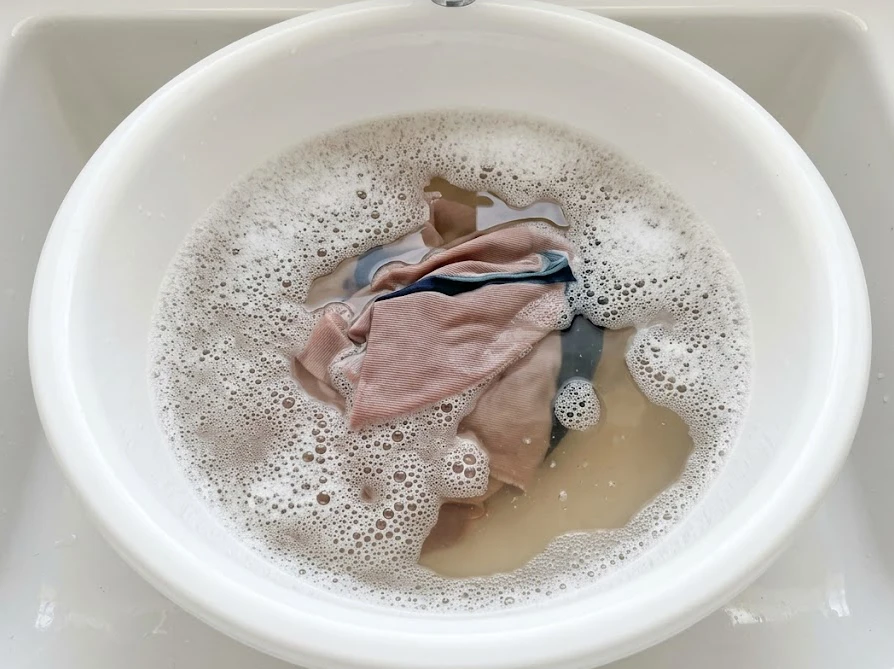 時間がたった頑固なインク汚れを落とすために洗面器の温水で衣類をつけ置きしている様子