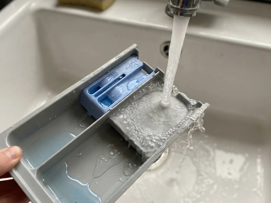 取り外した柔軟剤の自動投入ケースをぬるま湯で洗う様子